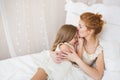 Portrait of mother kisses her little daughter on a bed