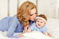 Portrait of mother and little baby girls with blue eyes in a striped blue dress lying on the bed. Mom gently kisses her daughter Royalty Free Stock Photo