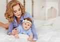 Portrait of mother and little baby girls with blue eyes in a striped blue dress lying on white bed. Mom tenderly looking at her d Royalty Free Stock Photo