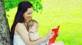 Portrait of mother and little girl baby reading book together on the grass under tree in summer park Royalty Free Stock Photo