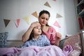 Mother looking after sick small daughter in bed at home, measuring temperature.