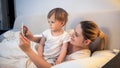 Portrait of young mother toddler son holding digital tablet in bed at night