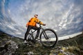 Portrait of the mountain cyclist standing with bike on the rocky hill against dramatic sky with clouds. Royalty Free Stock Photo