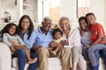Portrait Of Multi-Generation Family Sitting On Sofa At Home Smiling At Camera