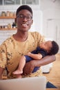 Portrait Of Multi-Tasking Father Holding Sleeping Baby Son And Working On Laptop Computer In Kitchen Royalty Free Stock Photo