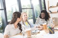 portrait of multiethnic cheerful businesswomen talking while sitting at workplace Royalty Free Stock Photo