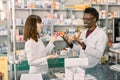 Portrait of multiethnical male and female pharmacists standing near pharmacy counter, talking, laughing and gesturing Royalty Free Stock Photo