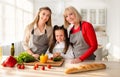 Portrait of multigenerational family with cute girl, her mom and granny posing in kitchen, smiling at camera Royalty Free Stock Photo