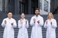 Portrait of a multiracial group of doctors standing outside a clinic in white coats applauding and smiling while looking Royalty Free Stock Photo