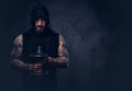 Portrait of a muscular bearded tattoed male wearing black sportswear with a hood, doing exercise with a dumbbell Royalty Free Stock Photo