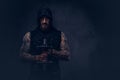 Portrait of a muscular bearded tattoed male wearing black sportswear with a hood, doing exercise with a dumbbell Royalty Free Stock Photo