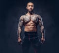 Portrait of a muscular naked bearded tattoed male with a stylish haircut in a sports trousers, isolated on a dark