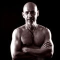 Portrait of a muscular topless bald middle-aged man with arms crossed on a black background