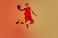 Portrait of muscular young man, basketball player in motion, throwing ball in a jump isolated over orange studio Royalty Free Stock Photo