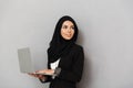 Portrait of muslim elegant woman 20s in black traditional clothing smiling and looking aside on copyspace while holding laptop, i Royalty Free Stock Photo