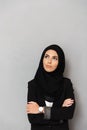 Portrait of muslim elegant woman 20s in black traditional clothing smiling and looking aside on copyspace, isolated over gray Royalty Free Stock Photo