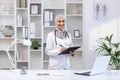 Portrait of a Muslim female doctor in a hijab standing in a modern office, holding a tablet with documents in her hands Royalty Free Stock Photo