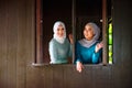 Portrait of Muslim Malay women wearing hijab and traditional costume during Aidilfitri celebrations at the wooden window of a