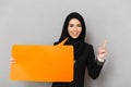 Portrait of muslim smiling woman 20s in black traditional clothing holding empty copyspace bubble for your text and pointing Royalty Free Stock Photo