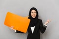 Portrait of muslim smiling woman 20s in black traditional clothing holding empty copyspace bubble for your text and gesturing han Royalty Free Stock Photo