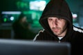 Portrait of mysterious hooded hacker sitting at desk and breaking into government data servers in dark Royalty Free Stock Photo
