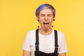 Portrait of naughty hipster woman sticking out tongue and keeping eyes closed. yellow background, studio shot Royalty Free Stock Photo