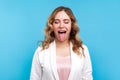 Portrait of naughty positive woman standing with closed eyes and demonstrating tongue. studio shot, blue background Royalty Free Stock Photo