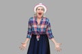 Portrait of nervous aggressive stylish mature woman in casual style with hat standing, raised arms with angry face and looking at Royalty Free Stock Photo