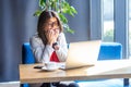 Portrait of nervous beautiful stylish brunette young woman in glasses sitting and looking at laptop monitor, bitting her nails and