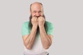 Portrait of nervous middle aged bald man with long beard in light green t-shirt standing, bitting his nails and looking at camera Royalty Free Stock Photo