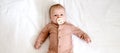 Portrait of a newborn baby girl who lies on a bed with a nipple soother. Three-month-old girl in brown suit lies on a
