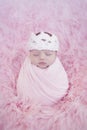 Portrait of newborn baby girl wrapped in pink wrap with knitted woolen crown headband. Infant on furry fluffy background Royalty Free Stock Photo