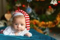 Portrait of a newborn child in a striped cap against the background of a Christmas tree. Astonished newborn baby with Royalty Free Stock Photo