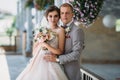 Portrait of newlyweds on wedding day. The groom in a gray suit with a white shirt and a bow tie hugs a beautiful bride