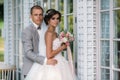 Portrait of newlyweds on wedding day. The groom in a gray suit with a white shirt and a bow tie hugs a beautiful bride