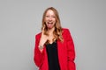 Portrait of nice, attractive, crazy young blonde woman, showing tongue out and rock-n-roll sign, standing in red blazer against Royalty Free Stock Photo