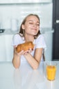 Portrait of nice woman eating croissant and drinking orange juice at table in kitchen interior while having breakfast at home Royalty Free Stock Photo