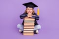 Portrait of nice cheerful schoolboy wearing hat sitting with pile book isolated over purple violet color background Royalty Free Stock Photo
