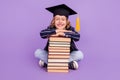 Portrait of nice cheerful schoolboy wearing hat sitting with pile book  over purple violet color background Royalty Free Stock Photo