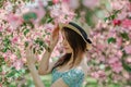 Portrait of nice young girl holding straw hat, in front of blooming pink apple garden, profile view Royalty Free Stock Photo