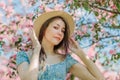 Portrait of nice young girl holding straw hat in front of blue sky and surrounded by blooming apple tree Royalty Free Stock Photo