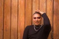 Portrait of non-binary person, young and South American, heavily make up and eyes closed, with one hand on head with wooden wall