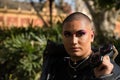 Portrait of non-binary person, young and South American, heavily make up, with sunglasses in hand and surrounded by greenery.