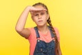 Portrait of nosy attentive serious little girl in denim overalls holding hand over eyes and looking far away Royalty Free Stock Photo