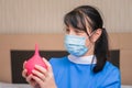 Portrait of a nurse in a medical mask with a red enema in hands. A woman in medical uniform is preparing to do a wash to the