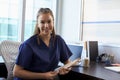 Portrait Of Nurse Wearing Scrubs Sitting At Desk In Office