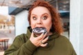 Portrait of obesed amazement woman eating a chocolate donut. The concept of diet and obesity