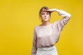 Portrait of observant beautiful young woman with fair hair in casual beige blouse, isolated on yellow background