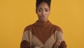 Portrait of offended afro-american girl in cozy sweater with crossed hands sadly looking aside over yellow background