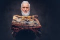 Tattooed elderly butcher with apron holding huge meat piece